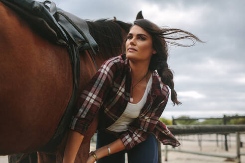 Junge Frau schirrt ein Pferd im Stall an. Cowgirl macht sich zum Reiten bereit. - JLPSF20550