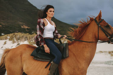 Attraktive junge Frau reitet abends am Strand auf einem Pferd. Cowgirl reitet mit ihrem Hengst am Meeresufer. - JLPSF20562