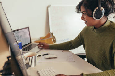 Programmiererin bei der Arbeit im Büro: Frau schaut auf ihren Laptop, während sie auf einem Desktop-Computer programmiert. - JLPSF20588