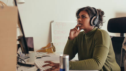 Junge Frau arbeitet an einem Computer in einem Büro eines Tech-Startups. Eine Programmiererin sitzt am Schreibtisch und schaut nachdenklich weg. - JLPSF20589