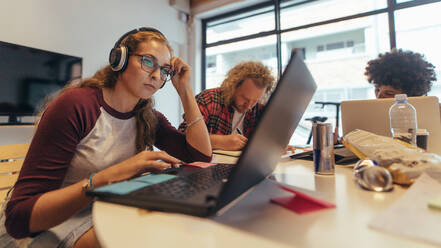 Eine weibliche Fachkraft arbeitet an einem Laptop mit Kollegen im Hintergrund. Software-Ingenieure arbeiten im Coworking Space eines Start-ups. - JLPSF20619