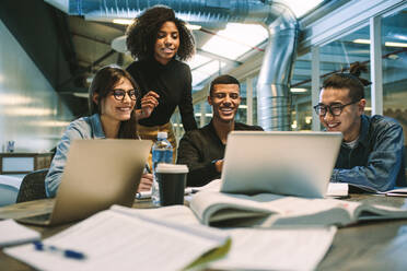 Eine Gruppe junger Studenten, die zusammen lernen und einen Laptop benutzen. Universitätsstudenten, die lächeln und einen Laptop in der Universitätsbibliothek benutzen. - JLPSF20653
