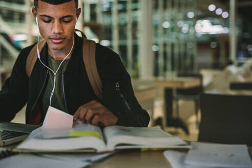 Männlicher Student sitzt am Tisch und liest Bücher und bereitet sich auf Prüfungen vor. Junger Mann liest ein Buch in der Universitätsbibliothek. - JLPSF20655