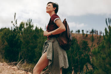 Glückliche Frau beim Wandern im Wald. Frau trägt eine Tasche und geht durch den Wald mit Bäumen im Hintergrund - JLPSF20665