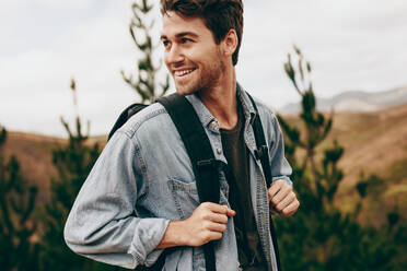 Man walking through a forest wearing a jacket and backpack. Happy man on a holiday hiking in a countryside location. - JLPSF20669