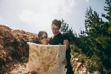 Man and woman holding a navigation map while hiking in a forest. Tourist couple using a map to find the route to their destination. - JLPSF20679