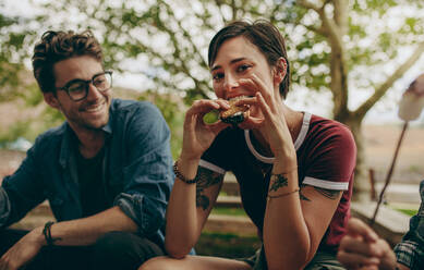 Glückliches Paar, das auf dem Land zeltet und Snacks isst. Touristisches Paar im Urlaub, das im Freien sitzend Snacks isst. - JLPSF20687