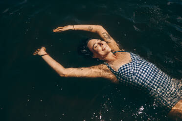 Lächelnde Frau im Urlaub, die sich beim Schwimmen im See entspannt. Frau im Bikini schwimmt im Wasser und schaut nach oben. - JLPSF20700