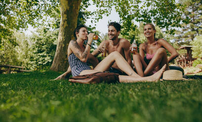 Zwei Frauen und ein Mann sitzen zusammen im Park und halten Bier. Freunde haben Spaß beim Biertrinken im Park. - JLPSF20705