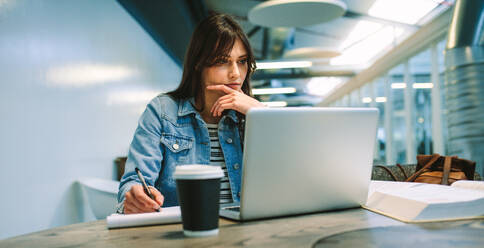 Clevere Studentin macht sich Notizen von Online-Informationen auf dem Laptop. Frau studiert auf dem Universitätscampus. - JLPSF20713