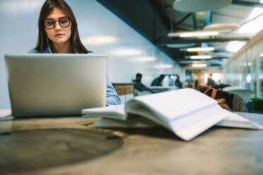 Frau mit Brille arbeitet an einem Laptop auf einem College-Campus. Studentin studiert auf einem Universitätscampus. - JLPSF20714