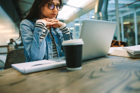 Frau, die in der Cafeteria eines Colleges sitzt und Informationen auf einem Laptop liest. Studentin, die in der Universitätsbibliothek auf einen Laptop schaut. - JLPSF20715
