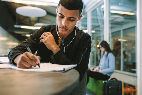 Junger Mann macht sich Notizen in einem Buch. Männlicher Student bereitet sich in der Universitätsbibliothek auf Prüfungen vor. - JLPSF20733