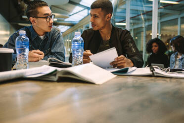 Zwei junge Studenten arbeiten gemeinsam an einer Aufgabe. Klassenkameraden sitzen mit Büchern an einem Tisch und diskutieren. - JLPSF20735