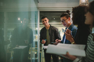 Eine Gruppe von Studenten steht gemeinsam mit Büchern an der Tafel. Multiethnische Universitätsstudenten während eines Workshops. - JLPSF20743