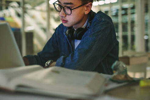Junger Student sitzt in der Bibliothek mit Laptop im College. Männlicher Student studiert in der Universitätsbibliothek. - JLPSF20752