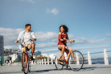 Happy man and woman riding bicycles in the street. Smiling couple enjoying riding on bicycles on a sunny day looking at each other. - JLPSF20768