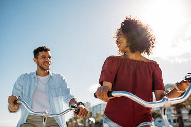 Ein glücklicher Mann und eine Frau fahren an einem sonnigen Tag Fahrrad. Ein Touristenpaar fährt auf Fahrrädern durch die Stadt. - JLPSF20772