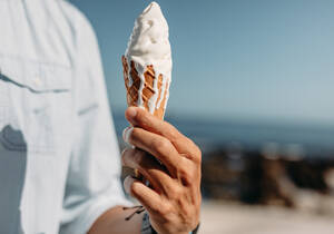 Nahaufnahme der Hand eines Mannes, der eine schmelzende Eistüte hält. Mann hält ein Eis an einem sonnigen Tag. - JLPSF20778