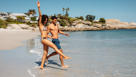 Excited woman walking in the water on the beach with her boyfriend. Man and woman having fun at the beach. - JLPSF20794