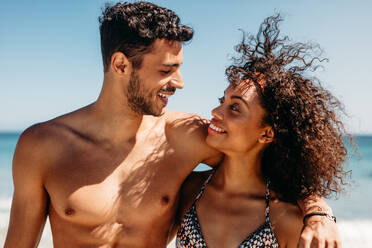 Happy tourist couple standing at the beach looking at each other. Couple in love spending time together at the beach. - JLPSF20800