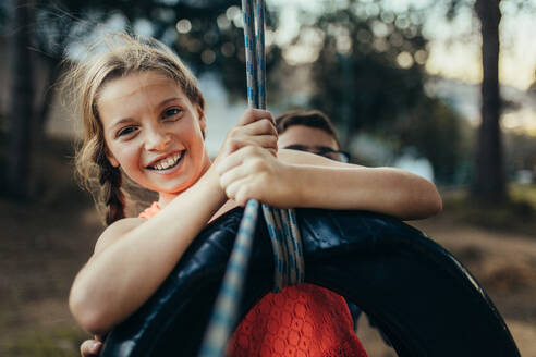 Young girl swinging on a tyre swing in a park. Kids having fun playing on a tyre swing in a park. - JLPSF20813