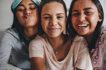 Three young girls sitting together posing for a selfie during a sleepover. Girls having a good time during a sleepover. - JLPSF20843