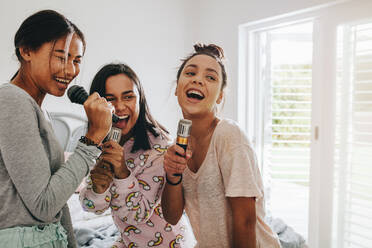 Mädchen, die zu Hause mit Mikrofonen in der Hand Lieder singen und Spaß dabei haben. Drei junge Mädchen, die bei einer Übernachtung Karaoke singen. - JLPSF20854