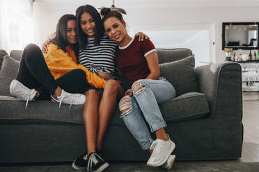 Drei Mädchen im Teenageralter sitzen zusammen und halten sich gegenseitig auf einer Couch. Mädchen sitzen auf einem Sofa im Wohnzimmer. - JLPSF20880