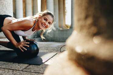 Fröhliche Frau beim Fitnesstraining mit einem Medizinball. Fitness-Frau macht Liegestütze auf einer Yogamatte. - JLPSF20904