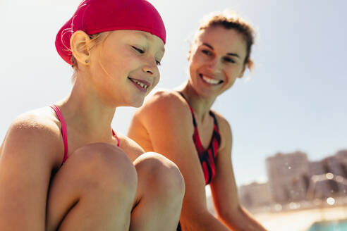 Mädchen sitzt mit ihrem Schwimmtrainer am Beckenrand. Lächelndes Kind mit Schwimmtrainer. - JLPSF20910