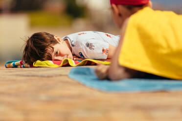 Junge und Mädchen liegen nach dem Schwimmunterricht auf einem Handtuch am Pool. Kinder ruhen sich nach dem Schwimmunterricht aus. - JLPSF20911