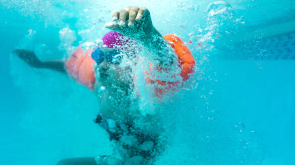 Unterwasseraufnahme eines Jungen mit Schwimmflügeln, der in ein Schwimmbecken springt. Junge nach dem Sprung in ein Schwimmbecken. - JLPSF20918