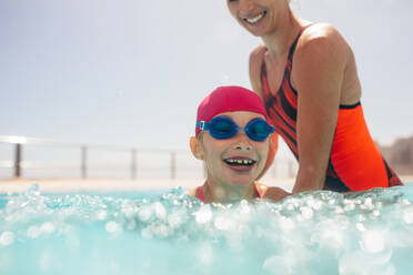 Mädchen bekommt Schwimmunterricht in einem Freibad mit ihrer Mutter. Mädchen mit Badekappe und Schwimmbrille lernt mit Hilfe der Mutter schwimmen. - JLPSF20924