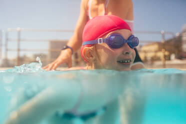 Nettes Mädchen, das mit einem Trainer im Freizeitzentrum schwimmen lernt. Mädchen, das mit dem Trainer Schwimmunterricht im Schwimmbad hat. - JLPSF20930