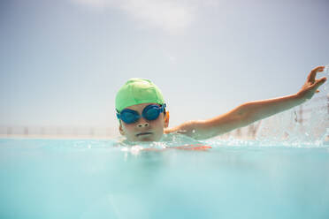Junge mit Badekappe und Schwimmbrille übt Schwimmen im Freibad. Junge lernt an einem Sommertag schwimmen. - JLPSF20931