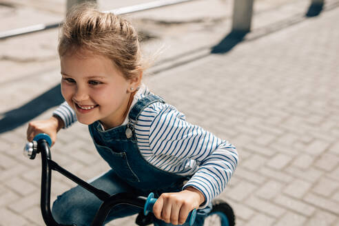 Nahaufnahme eines fröhlichen kleinen Mädchens, das sich beim Fahrradfahren im Freien vergnügt. Junges Mädchen fährt mit dem Fahrrad auf der Straße. - JLPSF20938