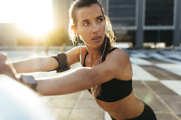 Nahaufnahme einer Sportlerin, die im Freien trainiert und dabei über Kopfhörer Musik hört. Fitness-Frau beim morgendlichen Workout mit Sonnenschein im Hintergrund. - JLPSF20949
