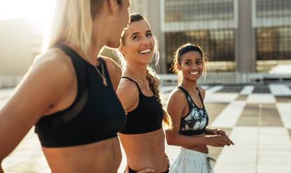 Drei Frauen in Trainingskleidung lächeln während ihres morgendlichen Workouts. Fitness-Frauen bei Aufwärmübungen vor ihrem morgendlichen Lauf. - JLPSF20952