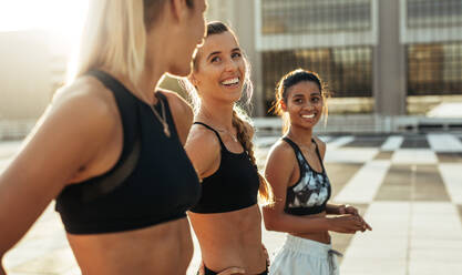 Three women in training clothes smiling during their workout in the morning. Fitness women doing warm up exercises before their morning run. - JLPSF20952