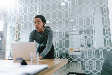 Young businesswoman working on laptop and looking away. African office worker making a presentation in conference room. - JLPSF21009