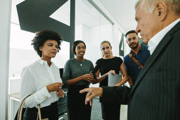 Ein junges Team von Geschäftsleuten hört den Ratschlägen eines leitenden Angestellten im Büroflur zu. Eine Gruppe von Geschäftsleuten unterhält sich im Büroflur. - JLPSF21029