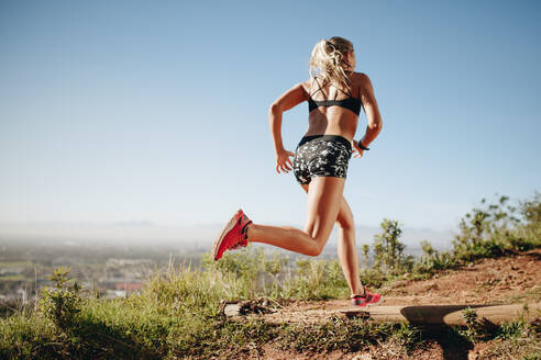 Rückansicht einer Frau in Fitnesskleidung beim Sprinten. Weibliche Athletin beim Training im Freien an einem sonnigen Tag. - JLPSF21047