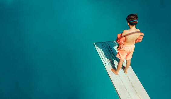 Draufsicht auf einen Jungen, der auf einem Sprungbrett steht und während des Schwimmunterrichts an einem Sommertag tauchen lernt. Junge lernt Schwimmen im Freibad. - JLPSF21083