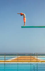 Junge steht auf einem Sprungturm und will ins Schwimmbad springen. Junge steht auf einem Sprungbrett und will springen. - JLPSF21084