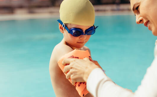 Eine Frau zieht einem Jungen Schwimmflügel an. Ein Junge macht sich am Pool für den Schwimmunterricht bereit. Eine Frau hilft ihrem Sohn, Schwimmflügel am Pool anzuziehen. - JLPSF21089