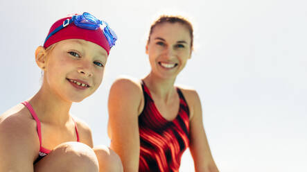 Lächelndes Kind mit Schwimmtrainer vor hellem Himmel, Mädchen und Trainer am Beckenrand. - JLPSF21101