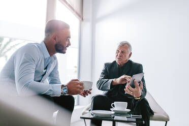 Zwei Geschäftsleute sitzen in der Büro-Lobby und diskutieren bei einer Tasse Kaffee über ihre Arbeit. Geschäftskollegen unterhalten sich während der Arbeitspause in der Büro-Lobby. - JLPSF21114