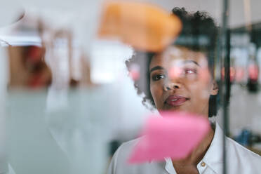 Businesswoman in meeting inside a wall cabin. Female executive looking sticky notes on transparent glass wall. - JLPSF21130