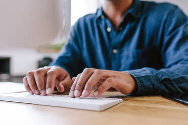 Nahaufnahme eines Geschäftsmannes, der an seinem Schreibtisch auf einer Tastatur tippt. Ausschnitt eines Mannes, der an einem Computer auf einem Bürotisch arbeitet. - JLPSF21140